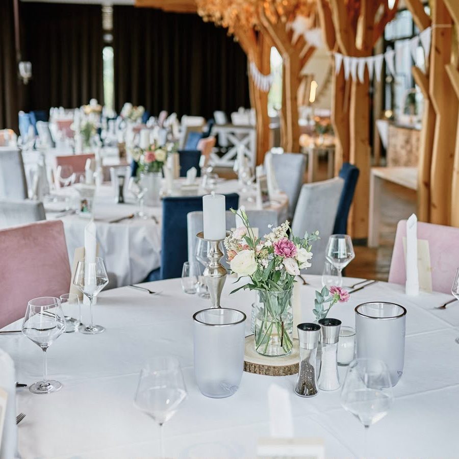Festlich eingedeckter Saal mit runden Tischen und floraler Dekoration