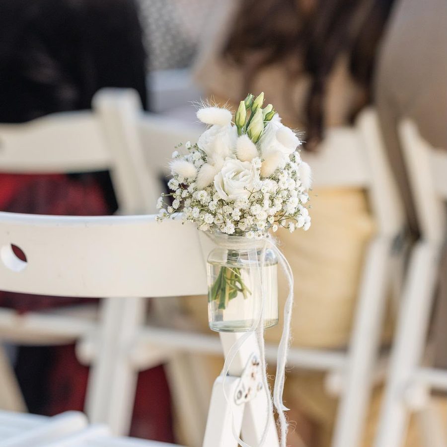 Kleines Blumenglas mit weißen Rosen am Stuhl der Trauung