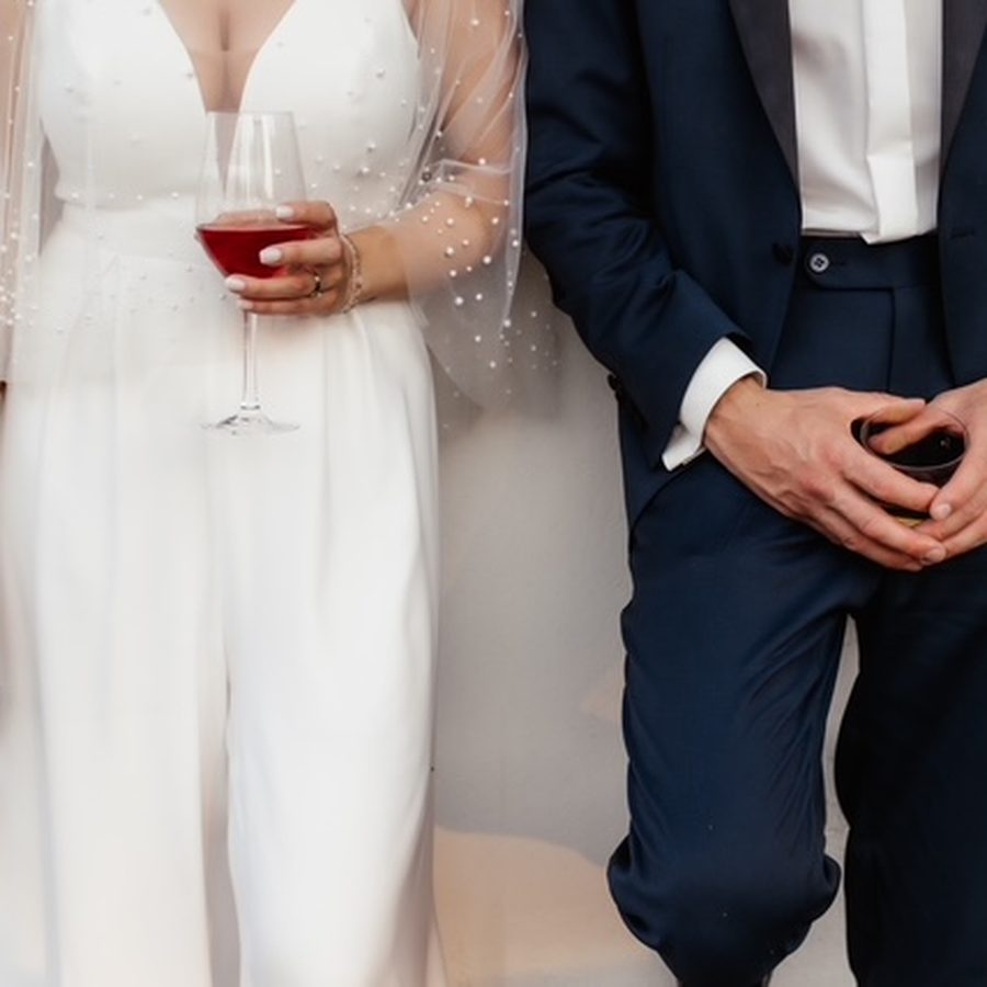 Brautpaar in Weiß und Dunkelblau mit einem Glas Wein